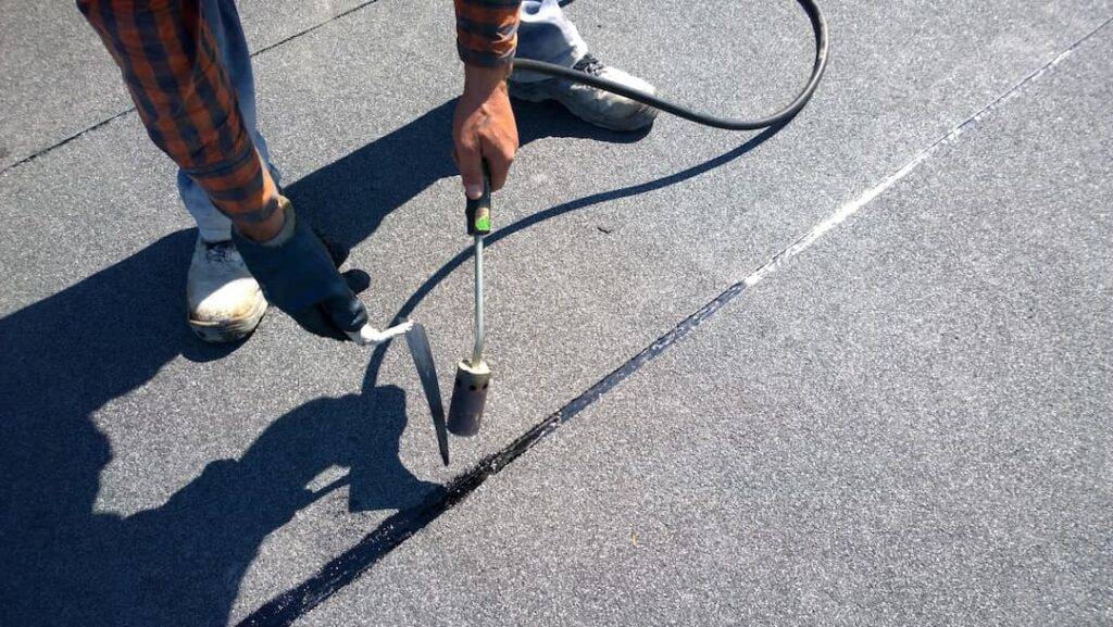 Roofer Preparing Part Of Bitumen Roofing Felt Roll For Melting By Gas Heater Torch Flame